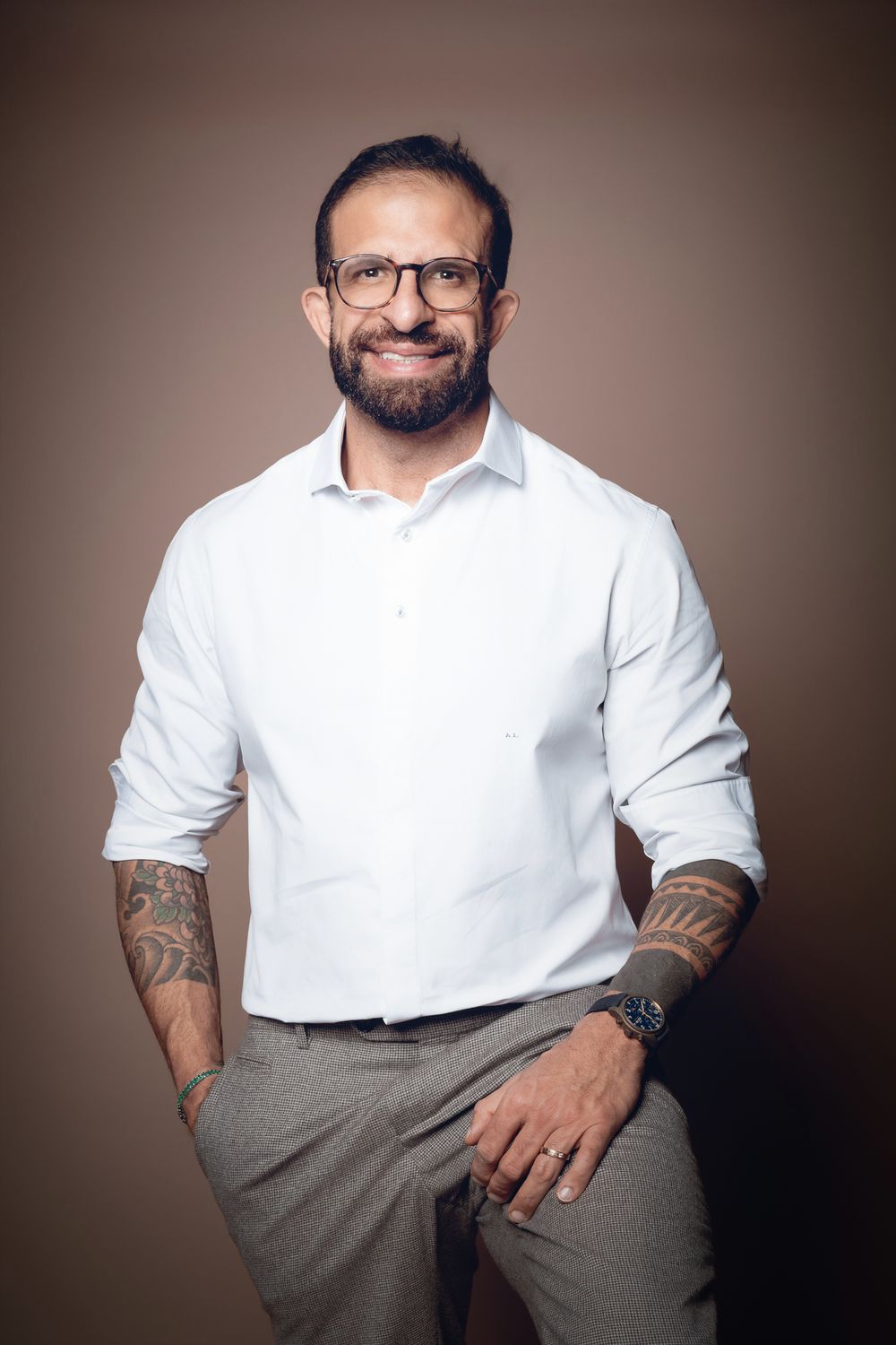 Dr. Adriano Lotfi de camisa branca, sorrindo, com tatuagens nos antebraços