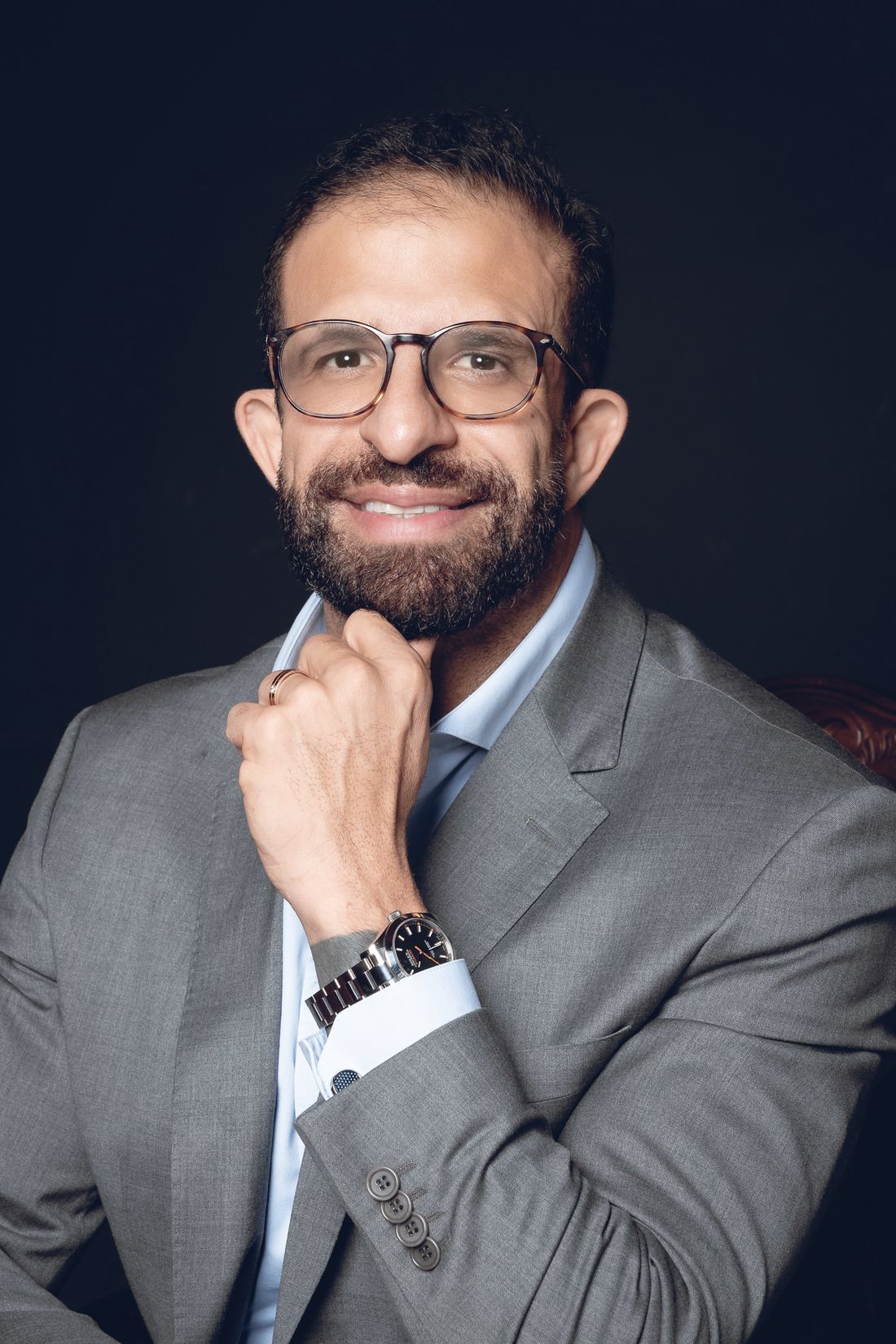 Dr. Adriano Lotfi, de terno cinza, sorrindo com a mão no queixo